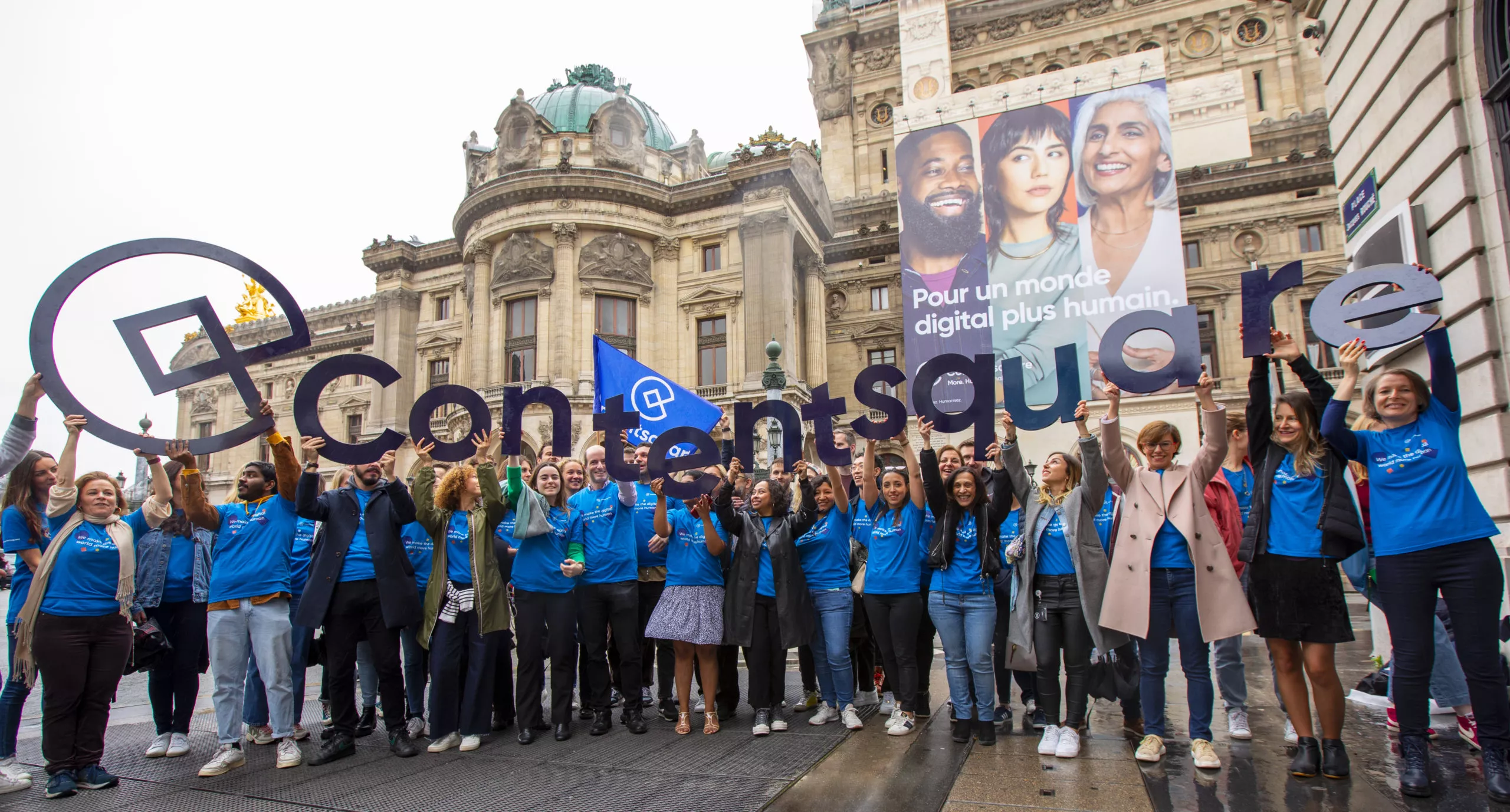 Contentsquare employees holding our logo above their heads in front of an advertisement banner in paris france